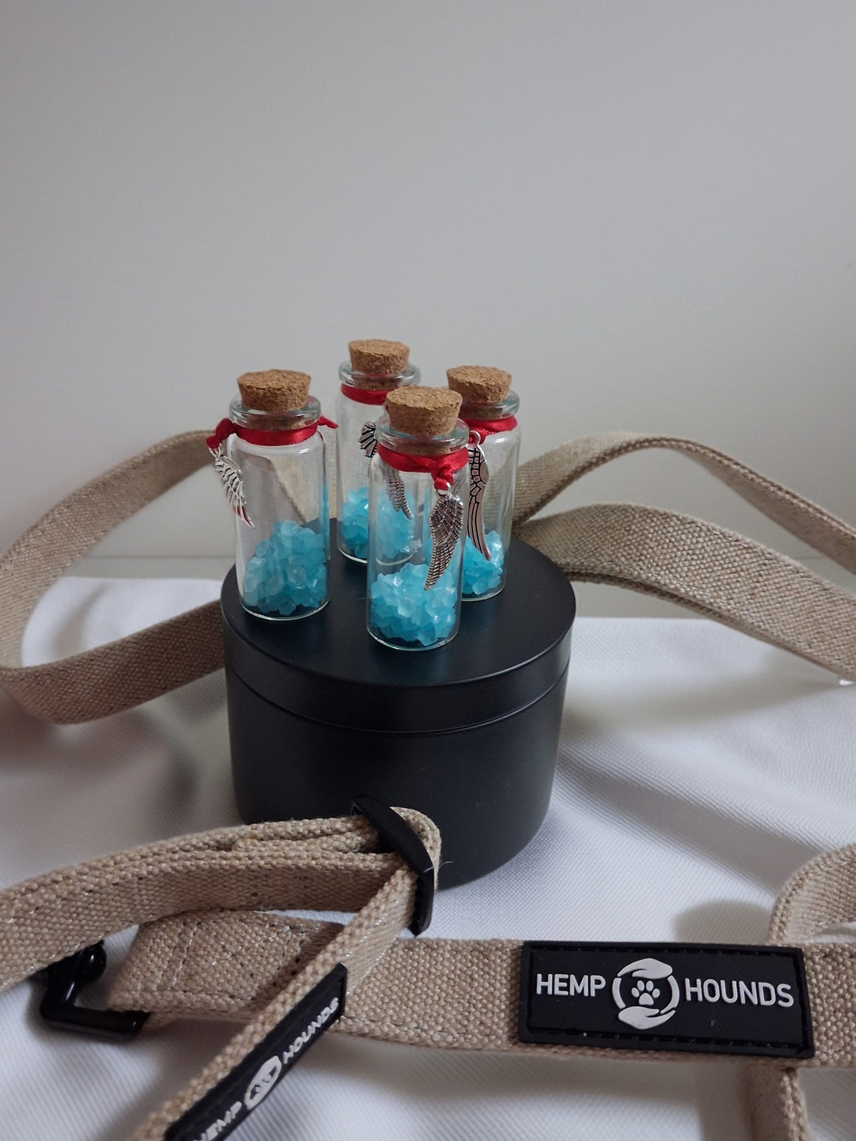 Four 5cm glass memorial keepsake bottles with cork lids, red ribbon and angel wing charms, filled with blue stones